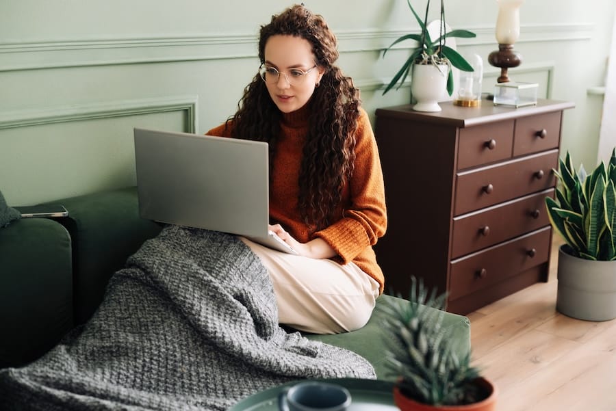 Woman on couch holding laptop engaging in online therapy.